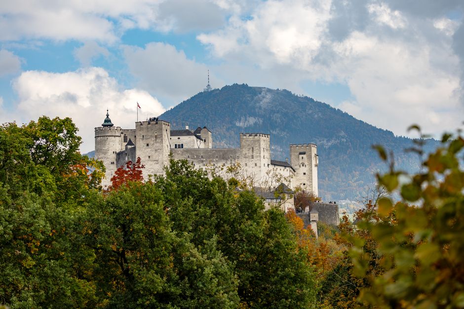 View of Hohensalzburg Fortress surrounded by fall foliage against a mountainous backdrop in Salzburg, Austria