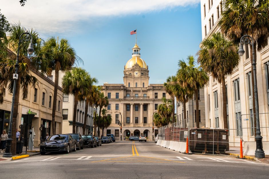 View of Savannah City Hall with its golden dome framed by palm trees along a downtown street