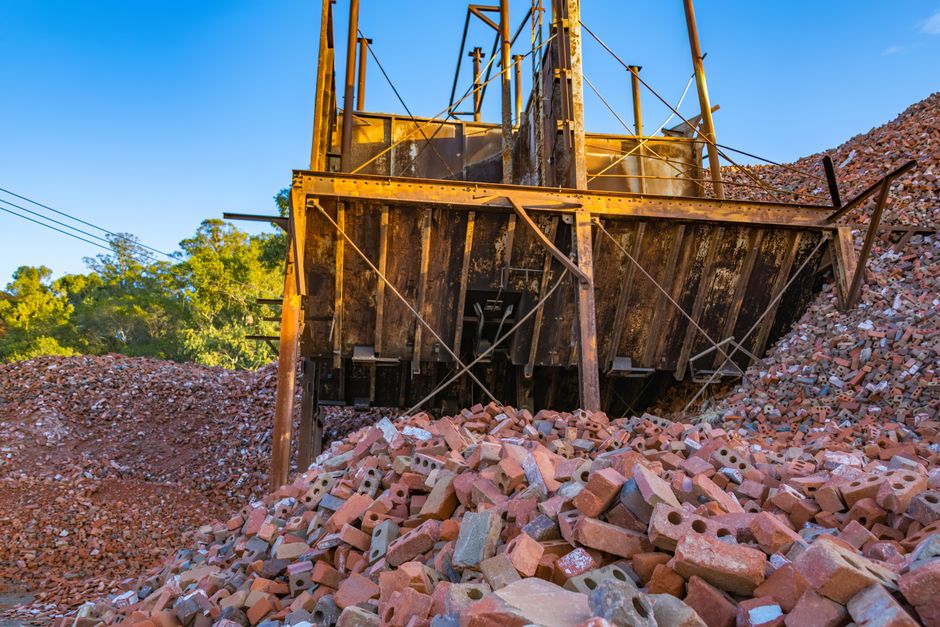 An abandoned pile of bricks with a rusty industrial structure outdoors under clear blue skies.