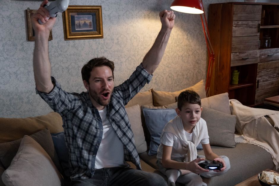 Father and son bond over video games in a cozy living room setting.