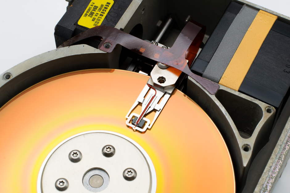 Detailed view of a vintage hard disk drive showing the read/write head and spinning platter.